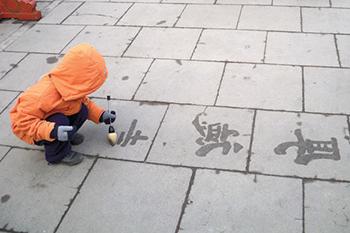 A child writing characters on a sidewalk.